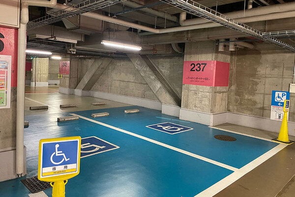 サンシャインシティ駐車場の地下2階のエレベーター付近にある、車いす専用の駐車スペースの写真、駐車スペースが青く塗られていて、車いすのピクトグラムが描かれており、駐車スペースの前には看板が立っていて、車いすのピクトグラムが記載されている