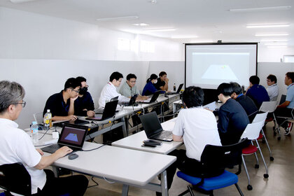 企業での講座の様子。会議スペースに並んだ受講者に尾野が説明している