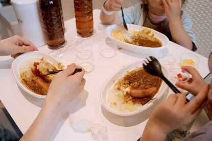 紙皿に盛られたカレーが3つ、テーブルの上に載っている。それを食べる女性と、二人のこどもの手元が写っている