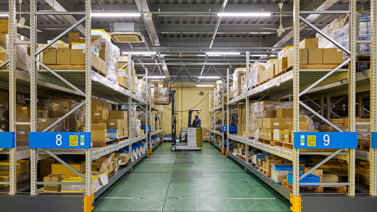 天井近くまである棚が左右に並んでおり、その真ん中に通路がある。通路の奥ではリフトが上段の棚の在庫を持ち上げている様子