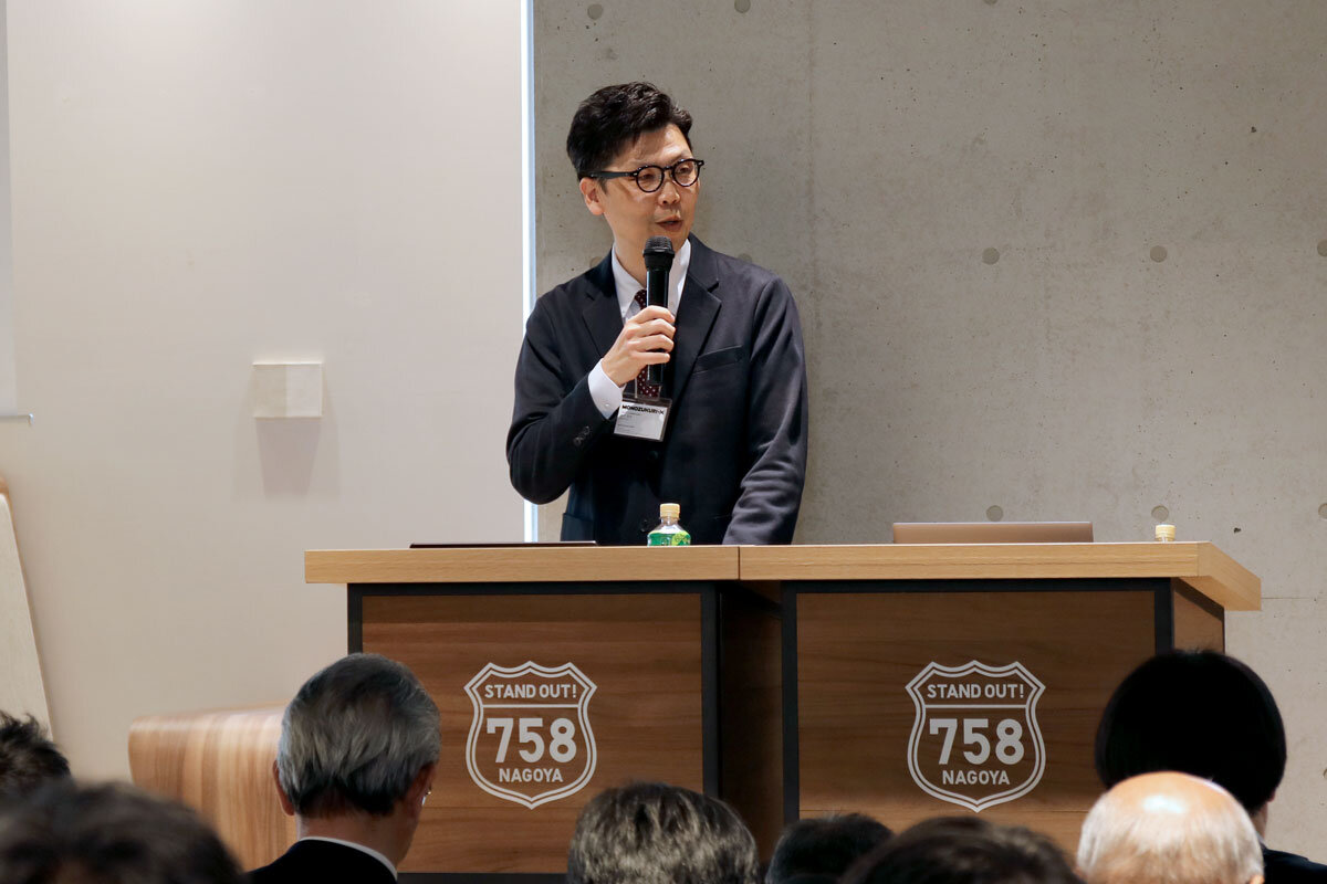 演壇に立ちマイクを手にしてしゃべっている石川浩司の姿