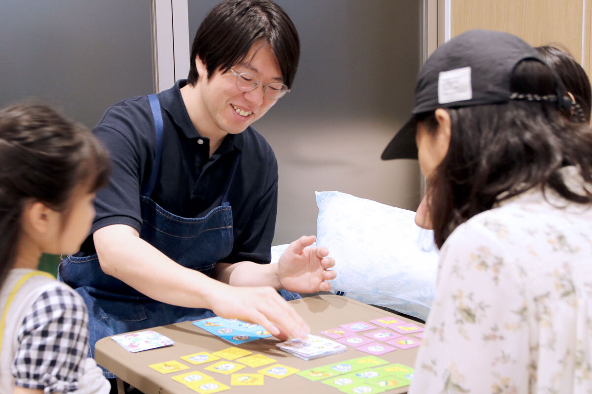子どもやその保護者と一緒にボードゲームをする加藤さんの様子