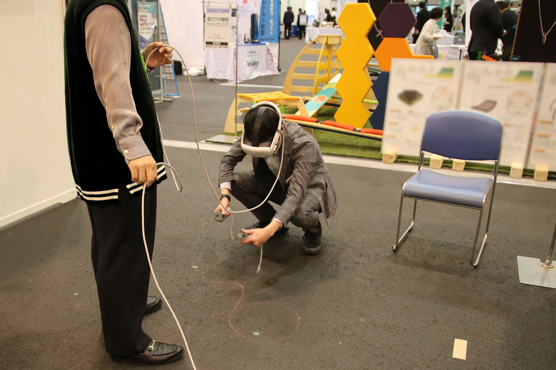 床にしゃがみこんでいる体験者の男性。両手にコントローラーを手にしてVR空間上の何かを操作している